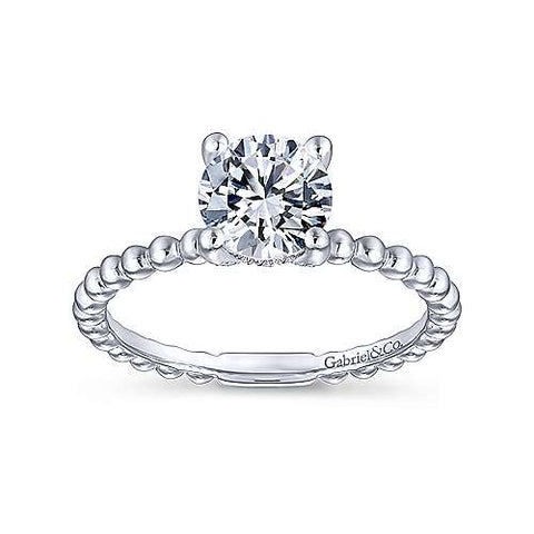 A beaded white gold band creates a distinctive backdrop for your round cut center stone. Dainty accent diamonds are hidden within the gallery.  